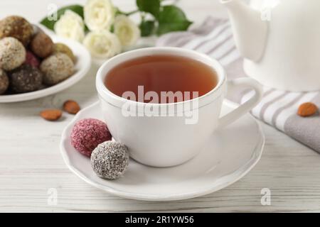 Tazza di tè aromatico e deliziose palle di caramelle vegane su un tavolo di legno bianco Foto Stock