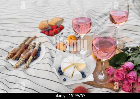 Bicchieri di delizioso vino rosa, fiori e cibo su coperta bianca da picnic Foto Stock