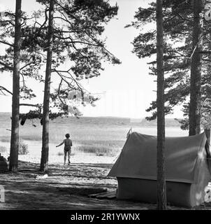 Campeggio nel 1960s. Un campeggio dove le famiglie trascorrono parte delle loro vacanze estive. Una tenda è sorto vicino alla spiaggia e una donna è visto correre verso l'acqua prendendo un bagno di raffreddamento questo giorno di estate. Värmland Svezia 1962. rif BV97-12 Foto Stock