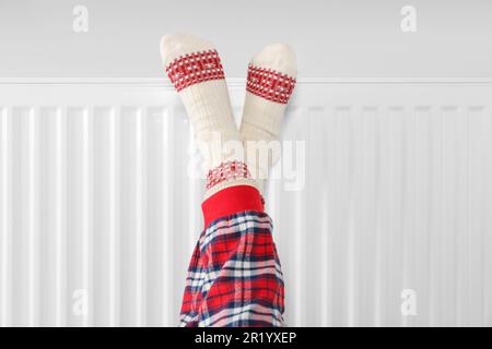 Bambina che scalda i piedi vicino al radiatore di riscaldamento interno, primo piano Foto Stock