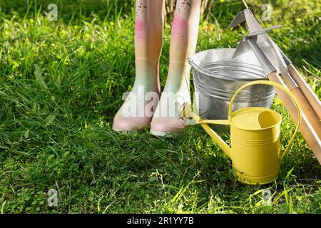 Annaffiatura lattina, attrezzi da giardinaggio e stivali di gomma su erba verde all'aperto Foto Stock