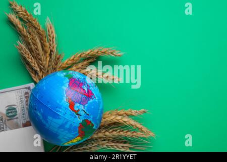 Concetto di importazione ed esportazione. Globo, spighe di grano e denaro su sfondo verde, piatto. Spazio per il testo Foto Stock