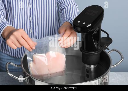 Donna che mette la carne confezionata sottovuoto in pentola con termostato a circolazione a immersione, primo piano. Cucina sous vide Foto Stock