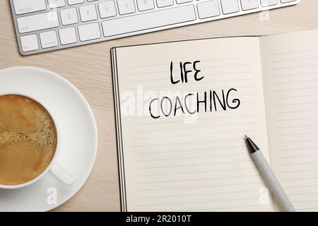 Frase Life Coach scritto in notebook, penna, tazza di caffè e tastiera su tavolo di legno, piatto Foto Stock