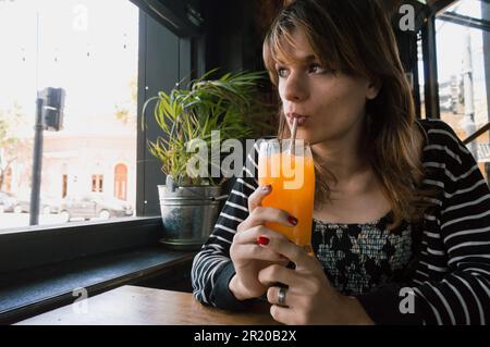 ritratto di giovane latina ispanica di etnia argentina, seduta bevendo succo d'arancia in un ristorante, in attesa del suo partner. Foto Stock