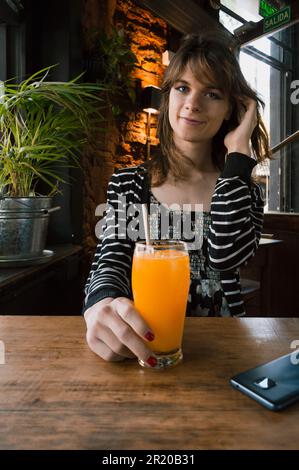 ritratto verticale giovane ispanica latina transgender donna di etnia argentina, seduta in un ristorante seduto, guardando la macchina fotografica. Foto Stock