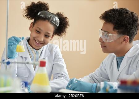 Ritratto di una ragazza nera sorridente che si diverse a scuola e a guardare la reazione chimica Foto Stock