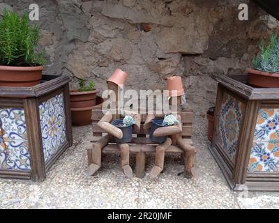 Bambole di legno sedute su una panca di legno. Circondato da pentole. A Medinaceli, a Soria. Fotografia. Foto Stock