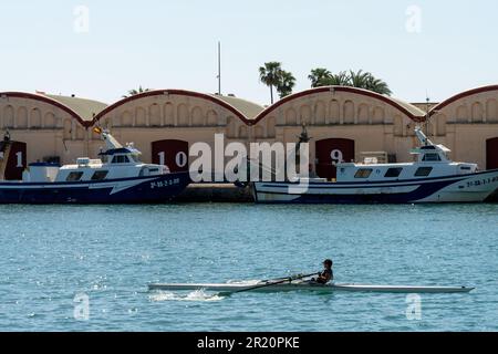 canoa nel porto con una barca da pesca sullo sfondo e gli edifici con i numeri 12 e 11 Foto Stock