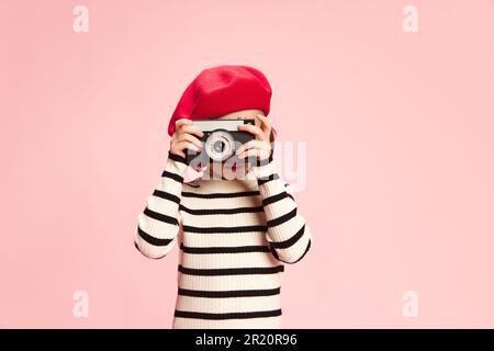 Ritratto di bambina, cild in maglione a righe e berretto rosso scattare foto con foto vintage camra agaisnt sfondo rosa studio Foto Stock