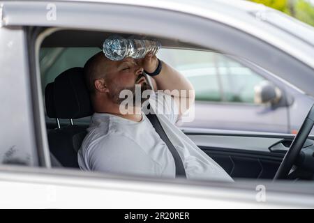 L'uomo stanco e sovrappeso guida l'auto con aria condizionata rotta in estate caldo tempo. Foto Stock