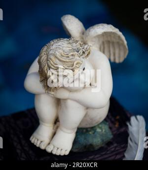 Un piccolo angelo figurina con ali bianche e piume è seduto in una posizione rilassata Foto Stock