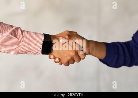 Uomini d'affari irriconoscibili che scuotono le mani su sfondo grigio Foto Stock
