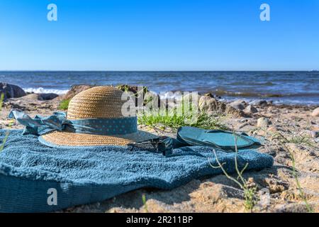 Cappello di paglia e infradito su un asciugamano blu su una spiaggia naturale, vacanze estive vicino alla località turistica Boltenhagen, Mar Baltico, Germania, copia spazio, vie Foto Stock