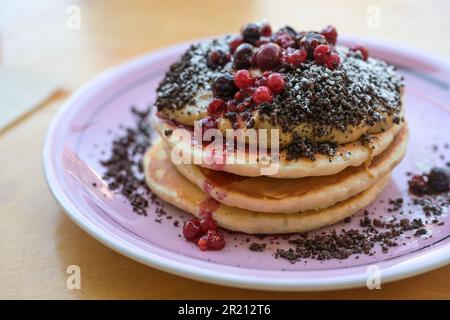 Frittelle impilate con crema al burro di arachidi, frutti di bosco, crumble e zucchero a velo su un piatto, colazione dolce, brunch o piatto da dessert, focus selezionato, narro Foto Stock