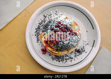 Frittelle con burro di arachidi, frutti di bosco, crumble e zucchero a velo su un piatto e un tavolo di legno, brunch dolce o piatto da dessert, vista dall'alto, Foto Stock