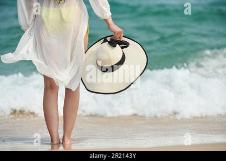 Giovane donna a piedi nudi in piedi su una spiaggia sabbiosa e godendosi le onde del mare Foto Stock