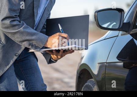 Agente assicurativo che ispeziona un'auto e prende appunti. Foto Stock