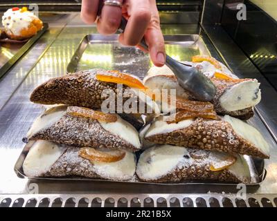 Pasticceria siciliana, una persona serve cannoli tradizionali con ricotta e arance candite. Un pasticciere prende alcuni dessert dal co refrigerato Foto Stock