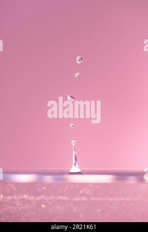 Le goccioline d'acqua cadono da vicino nell'acqua rosa, rendendola il centro perfetto nella natura Foto Stock