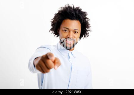 Attraente giovane ragazzo afro-americano allegro indossare camicia bianca punta indice dito alla fotocamera, scegliendo si isolato su sfondo bianco, felice uomo millenario mostrando direzione alla fotocamera Foto Stock