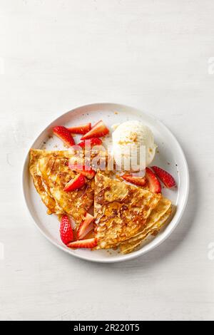 crepes decorato con miele, fragole e gelato su tavolo bianco, vista dall'alto Foto Stock