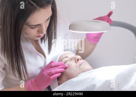 il cosmetologo esegue con perizia le procedure facciali sul cliente alla clinica estetica, compreso il peeling Foto Stock