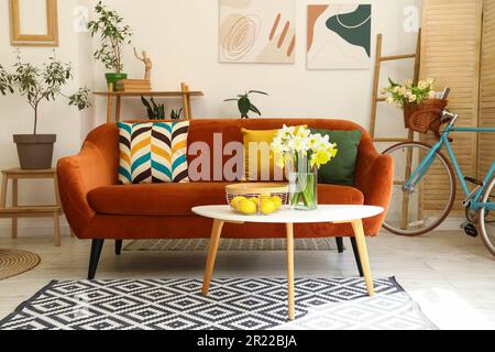 All'interno di un soggiorno luminoso con un comodo divano marrone e fiori narciso su un tavolino da caffè Foto Stock