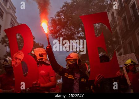 Madrid, Spagna. 16th maggio, 2023. Un vigile del fuoco tiene un flare mentre il resto dei manifestanti tiene cartelli che esprimono la loro opinione durante la dimostrazione. Dimostrazione dei vigili del fuoco spagnoli organizzata dalla Professional Firefighters Union (CUBP). I vigili del fuoco hanno annunciato che chiederanno l'approvazione di una legge quadro che distingua le loro funzioni e poteri, poiché hanno assicurato che attualmente ci sono molte comunità autonome che non hanno leggi che regolano la loro attività, lasciandole non protette. Credit: SOPA Images Limited/Alamy Live News Foto Stock