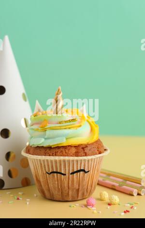 Dolcissimo cupcake unicorno e oggetti da festa sul tavolo giallo Foto Stock