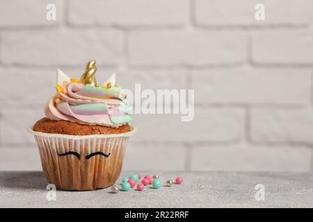 Dolce dolce cupcake unicorno su tavolo grigio chiaro, spazio per il testo Foto Stock