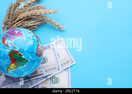 Concetto di importazione ed esportazione. Globo, spighe di grano e banconote su sfondo azzurro, piatto. Spazio per il testo Foto Stock