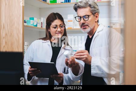 Fornitori di servizi sanitari che compilano prescrizioni online in farmacia. Due farmacisti maturi che leggono l'etichetta di un farmaco. Uomo e donna che lavorano insieme Foto Stock