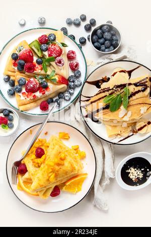 Varietà di crepes fresche con cioccolato, marmellata, frutta e frutti di bosco su sfondo bianco. Deliziose crepes fatte in casa. Vista dall'alto. Foto Stock