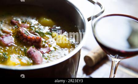 Pentola con polpo cotto stufato con patate e un bicchiere di vino rosso sul lato. Foto Stock