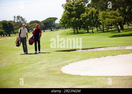 Che giorno impressionante per una partita di golf. due uomini che trasportano i loro sacchetti di golf attraverso un campo da golf. Foto Stock