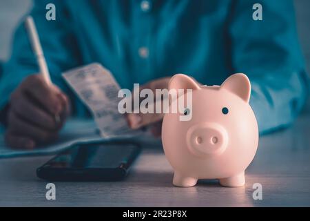 Il piggy bank del maiale rosa come concetto di risparmio con risparmio. Un uomo conta il suo reddito. Un giovane uomo d'affari al lavoro. Contabilità domestica Foto Stock