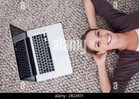 Connessi, ovunque e in qualsiasi momento. Scatto ad angolo alto di una giovane donna sdraiata sul pavimento con il suo notebook. Foto Stock