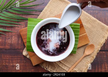 Budino di riso nero appiccicoso con taro e latte di cocco alla vista superiore della tavola di legno, riso glutinoso nero - dessert tailandese chiamato Khao Nieow Dam Foto Stock