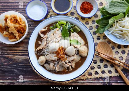 Zuppa di noodle in stile thailandese servita con piatto di verdure adagicato su un tavolo di legno - famoso cibo di strada, zuppa di noodle in barca thailandese Foto Stock