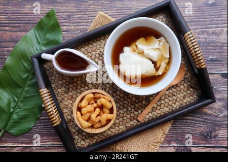 Douhua - soffice budino di tofu (cagliata di soia), famoso dessert sano asiatico servito in un vassoio di bambù di tavolo di legno alla vista dall'alto Foto Stock