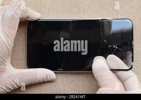 Mani che togliono la protezione in vetro rotta o la copertura dello schermo in pellicola dello smartphone - concetto di sicurezza e protezione Foto Stock