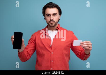 bruna intelligente 35 anni uomo millenario ben curato con capelli splendidi mostra un mock-up di una carta di credito e un telefono Foto Stock