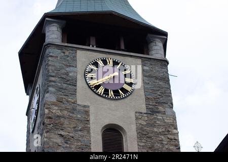 Il cielo mistoso abbraccia l'iconica torre dell'orologio nel villaggio di Zermatt, un mix di storia e fascino tranquillo nelle incantevoli Alpi svizzere. Foto Stock