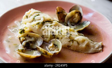 Nasello cotto con prezzemolo verde e salsa all'aglio servito con vongole. Ricetta spagnola tradizionale. Foto Stock