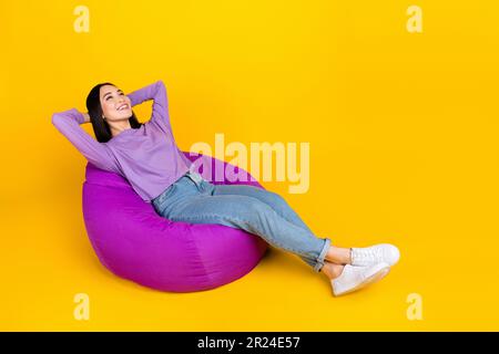 Foto a grandezza naturale di giovane donna cinese spensierata positiva sdraiata confortevole pouf mani rosa testa annegata isolato su sfondo di colore giallo Foto Stock