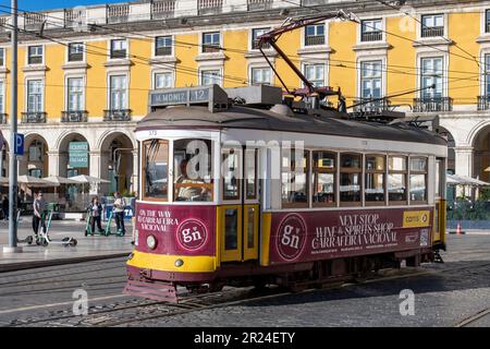 Lisbona, Portogallo-Ottobre 2022: Vista ravvicinata di un tram rosso su piazza Praha do Comércio con un tradizionale edificio di colore giallo Foto Stock