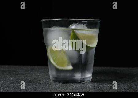 Bicchiere di vodka con fettine di lime e ghiaccio sul tavolo grigio Foto Stock