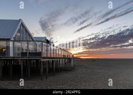 Vista panoramica del tramonto sulla spiaggia e sulle dune con padiglione a corda sull'isola di Texel nei Paesi Bassi con lunghe fasce di nuvola arancione Foto Stock