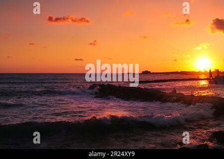 Una persona che osserva il tramonto sul mare nelle vicinanze del porto e del castello medievale di Paphos, Cipro Foto Stock